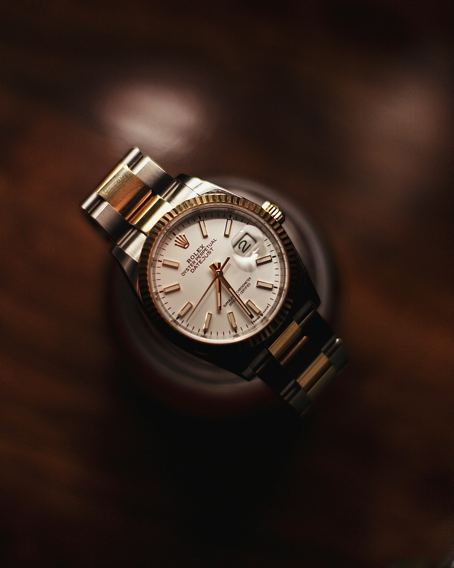 Close-up of a Rolex Datejust watch with a white dial, gold hour markers, and a two-tone gold and silver bracelet, displayed on a wooden surface.
