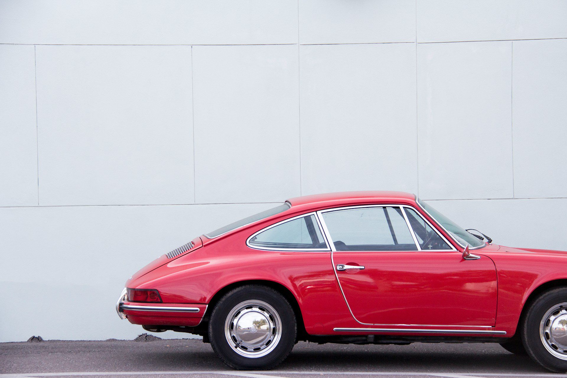 A vintage red Porsche 911 parked against a minimalist white wall.