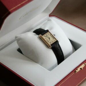 Vintage Gold Cartier Tank Watch in Red Box - New York Loan - New York Loan A vintage gold Cartier Tank watch with a black leather strap rests on a white cushion inside a red Cartier box.
