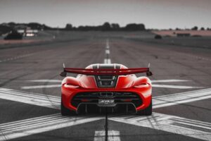 Rear view of a red high-performance sports car with a large rear wing on a deserted runway, tire marks visible on the asphalt.