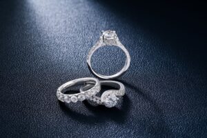 Diamond engagement ring with a central stone and pavé band on a dark textured surface.